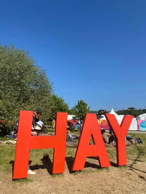 I’m standing with my son in a carrier behind the giant orange H A Y letters just outside the festival entrance
